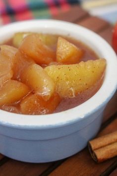 apples and cinnamon sticks sit in a bowl on a table next to an apple cider