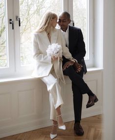 a man and woman sitting next to each other on a window sill with flowers in their hands