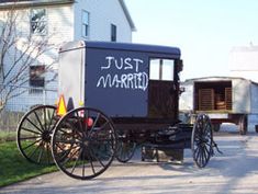 an old fashioned horse drawn carriage parked in front of a white building with just married written on it