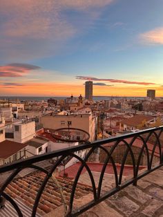 the sun is setting over an urban area with buildings and water in the distance, as seen from a balcony