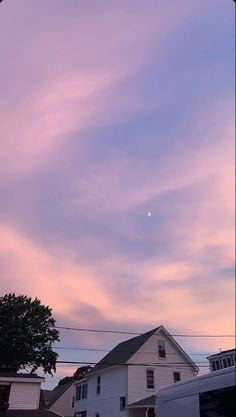 the sky is pink and purple as the sun goes down over houses in this neighborhood