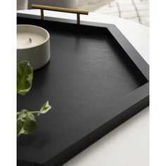 a black tray with a white bowl and a candle on the table next to it