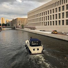 a white boat traveling down a river next to a tall building on a cloudy day