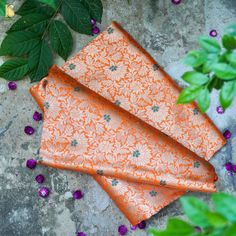 three orange napkins sitting on top of a cement floor next to green leaves and purple flowers