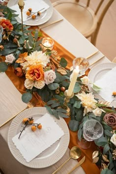 the table is set with white plates and gold place settings, orange napkins and flowers