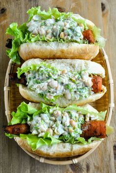 two hot dogs with lettuce and other toppings in buns on a wooden table