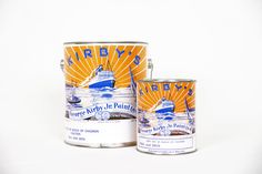 two tins of paint sitting next to each other on a white surface with an orange and blue boat in the background