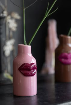 three vases with lipstick painted on them and flowers in the middle one is pink