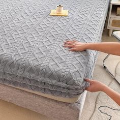 two hands reaching for the bottom of a bed that has been made with a mattress