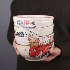 a person holding four bowls with different designs on them, all stacked in the same row