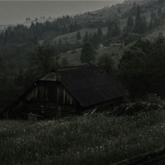 an old barn sits in the middle of a field with trees and hills behind it