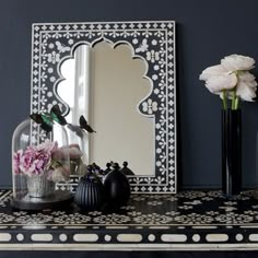 two black vases with flowers in them on a shelf next to a framed mirror