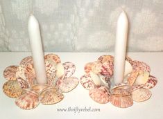 two candles with seashells on them sit next to each other in front of a white wall