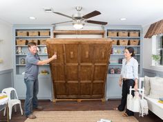 a man and woman standing in front of a large wooden cabinet with two fans on it