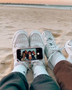 someone taking a selfie with their cell phone on the beach while wearing tennis shoes