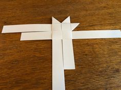 an origami cross made out of white paper on a wooden table with scissors