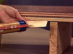 a person holding a piece of wood near a table with two pencils on it