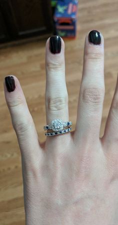 a woman's hand with black and white nail polish holding up her engagement ring