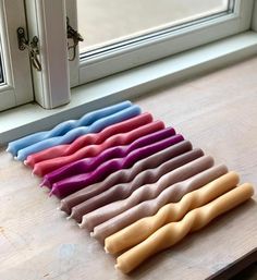 a bunch of different colored candles sitting on top of a wooden table next to a window