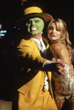 a man in a suit and tie standing next to a woman wearing a mask on her face