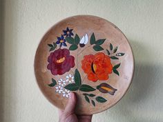 a hand holding a wooden plate with flowers painted on it