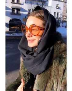 a woman wearing sunglasses and a fur coat in the snow with her head covered by a scarf