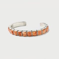 The Federico 20 Square Orange Spiney Oyster Cuff Bracelets offer a delicate, yet bold style with a 6mm sterling silver cuff that's studded with stunning stones. Crafted by renowned jewelry artisan Federico Jimenez, this beautiful cuff is a single row of rectangular cabochons of polished natural orange spiney oyster, set in simple sterling silver bezels. The straight-edged slim silhouette is perfect for incorporating into a stack. Born in 1941, jewelry artisan Federico Jimenez has long had an app Artisan Polished Bangle Jewelry, Sterling Silver Polished Cuff Jewelry, Luxury Oyster Cuff Bracelet As Gift, Sterling Silver Cuff Bracelet With Oyster Detail As Gift, Sterling Silver Cuff Oyster Bracelet As Gift, Sterling Silver Cuff Bracelet With Oyster Design, Collectible Silver Cuff Bracelet With Oyster Design, Formal Cuff Oyster Bracelet, Federico Jimenez Jewelry