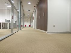 an empty office hallway with glass walls and carpet