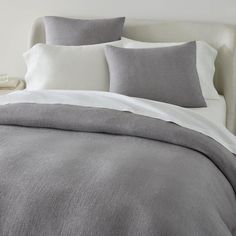 a bed with grey and white linens on top of it, next to a night stand