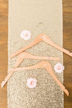 three wooden clothes hangers with flowers on them sitting on top of glittered fabric