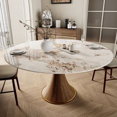 a marble dining table with two chairs and plates on the top, in front of a window