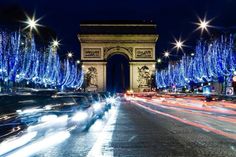 the arc de trioes is lit up with blue lights and christmas trees in front of it