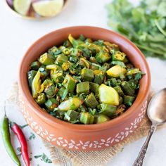 a bowl filled with green vegetables next to some red chili peppers and lime wedges