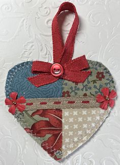 a patchwork heart ornament with red ribbon and flowered design on it