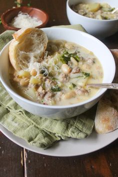 there is a bowl of soup on the table with bread and spoons next to it