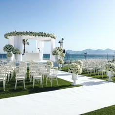 an outdoor ceremony set up with white chairs and flowers on the grass near the ocean