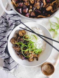 a white bowl filled with meat and rice next to chopsticks on a table