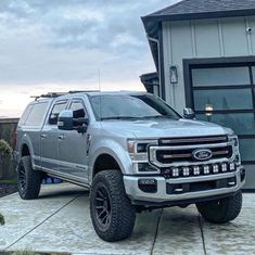 a silver truck is parked in front of a house with large tires on it's tires