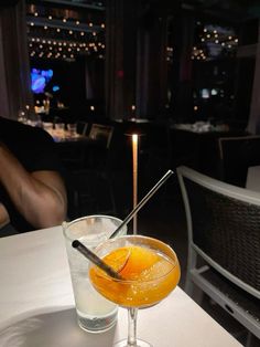 an orange cocktail sits on a table in a dimly lit room with people sitting at tables