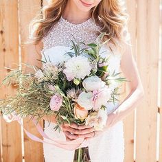 a woman holding a bouquet of flowers in her hands while standing next to a wooden fence