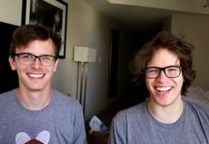 two young men standing next to each other in front of a mirror smiling at the camera