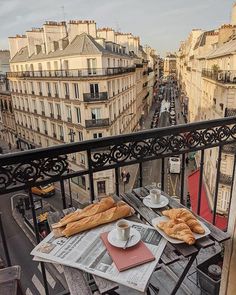 a table with bread and coffee on top of it in front of some tall buildings