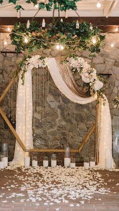 a stone wall with candles and flowers on it is decorated with greenery, white roses and hanging from the ceiling