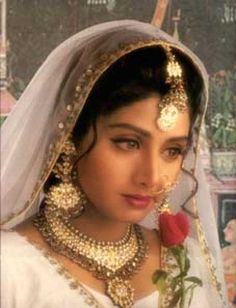 a woman wearing a bridal outfit and holding a rose in her right hand while looking at the camera