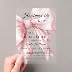 a person holding up a pink bow on top of a white card with the words she's tying the knot