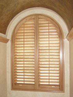 an arched window with wooden shutters in a room that has white walls and ceiling