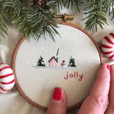 a hand embroidered christmas ornament with red and white balls on it, next to a pine tree