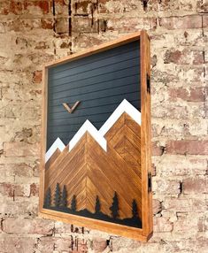 a wooden sign hanging on the side of a brick wall with mountains and trees painted on it