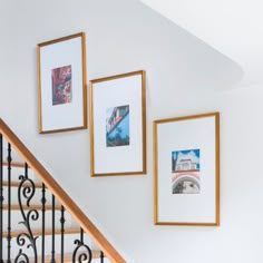 three framed photographs hang on the wall next to a stair case and hand rail with wrought iron railing