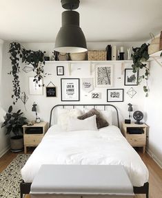 a white bed sitting in a bedroom next to a wall with pictures and plants on it